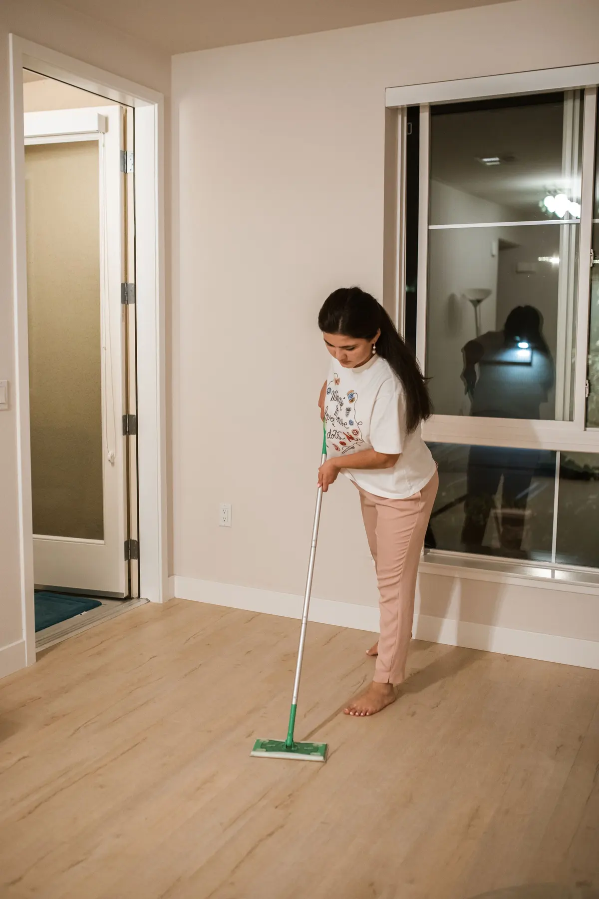 A woman sweeping a new light wood-look plank floor with a flat mop in an empty room
