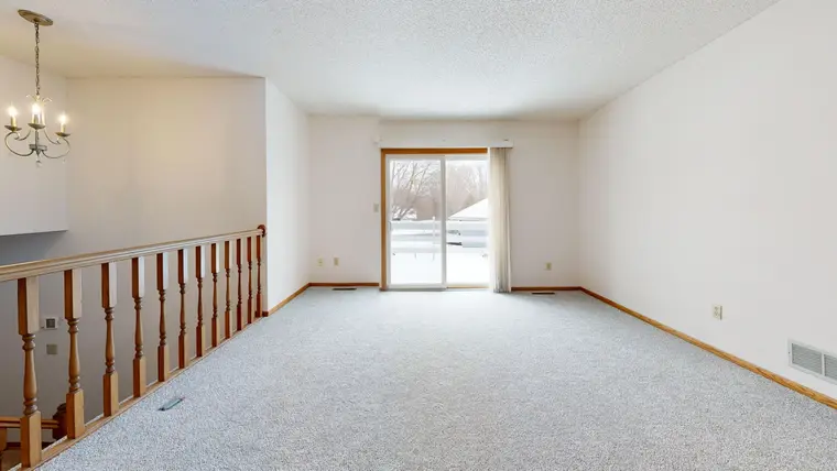 Empty living room with new carpet laid wall to wall under a chandelier
