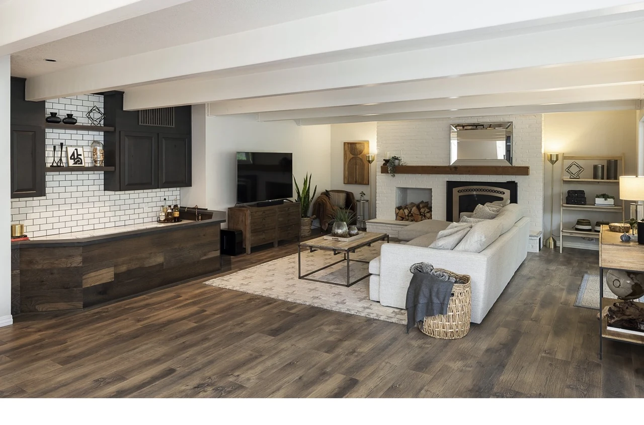 Open living room with wide-plank flooring, white beamed ceiling and a brick fireplace